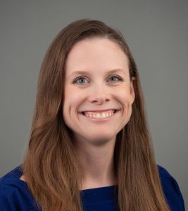 Portrait of a person with long brown hair and a blue top, smiling.