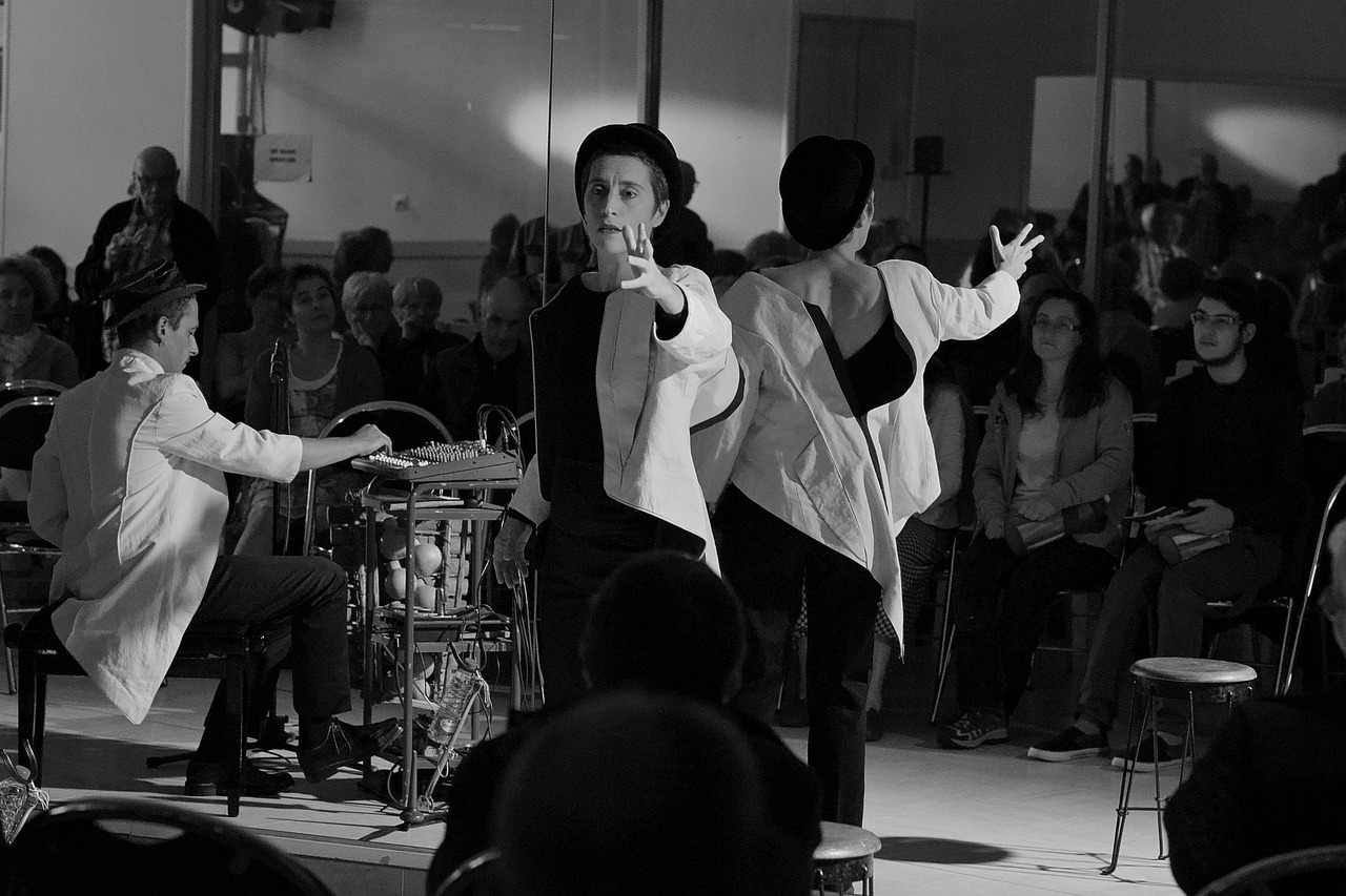 Black-and-white image of two performers and a musician in front of an audience.