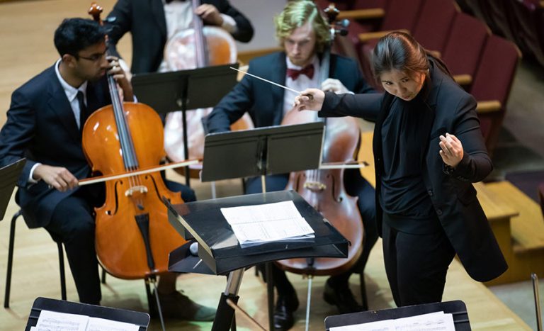 Conductor leading cellists during a performance in a concert hall.
