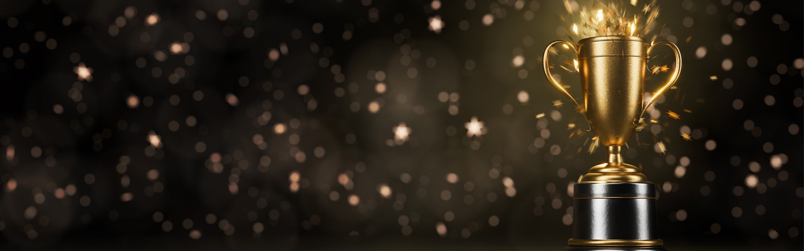 Gold trophy with sparkling light bursts on a dark background filled with bokeh lights