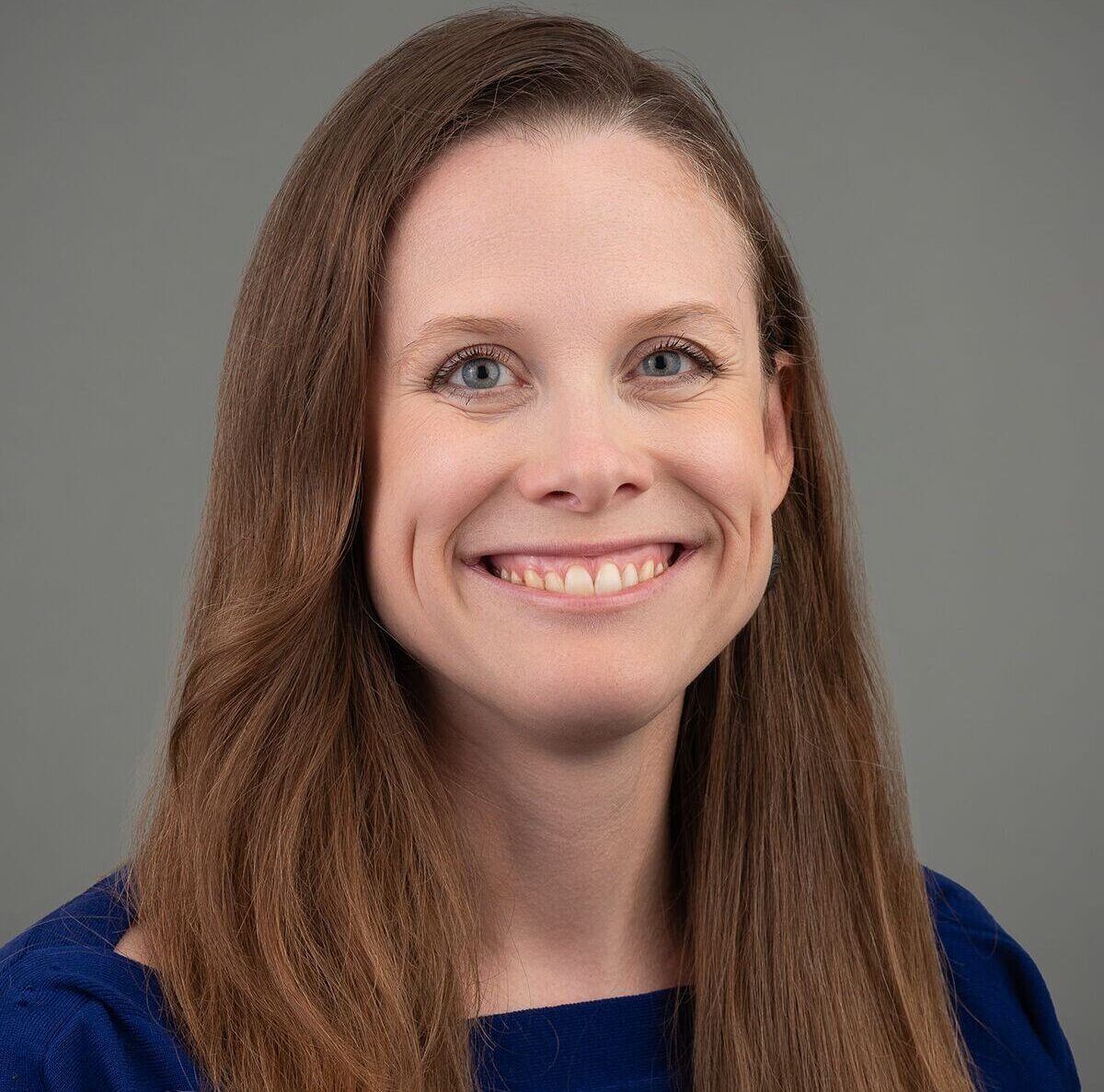 Portrait of a person with long brown hair and a blue top, smiling.